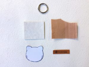 猫型のクッションフロア、フェルト、革タグ、カラビナを並べた制作パーツの写真